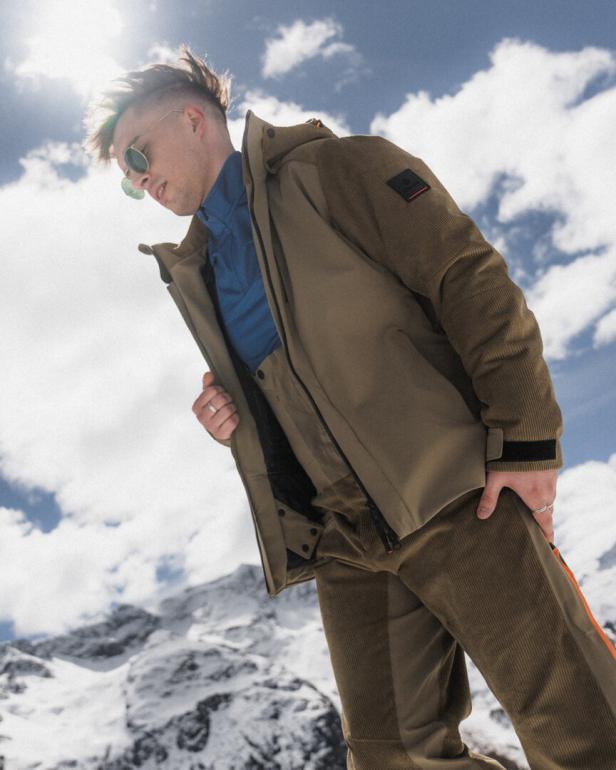 Ein Mann mit Sonnenbrille und Winterkleidung steht vor schneebedeckten Bergen.