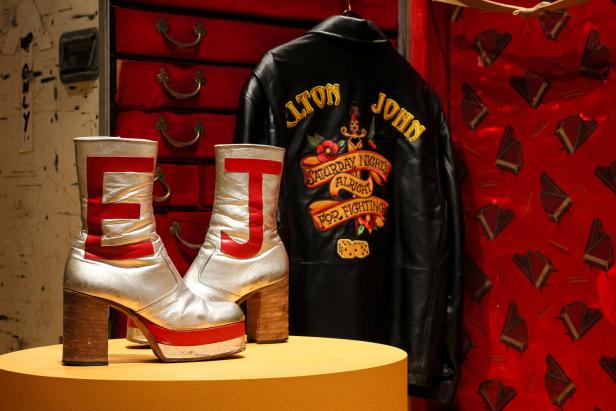 Ein Paar silberne Plateaustiefel mit rotem „J“ und eine Lederjacke von Elton John.