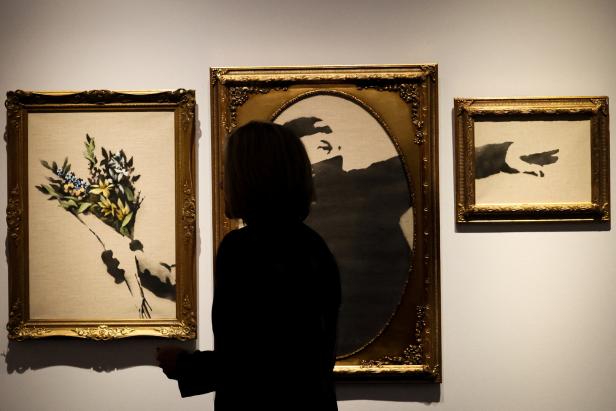 Eine Frau betrachtet drei gerahmte Banksy-Gemälde in einer Kunstgalerie.