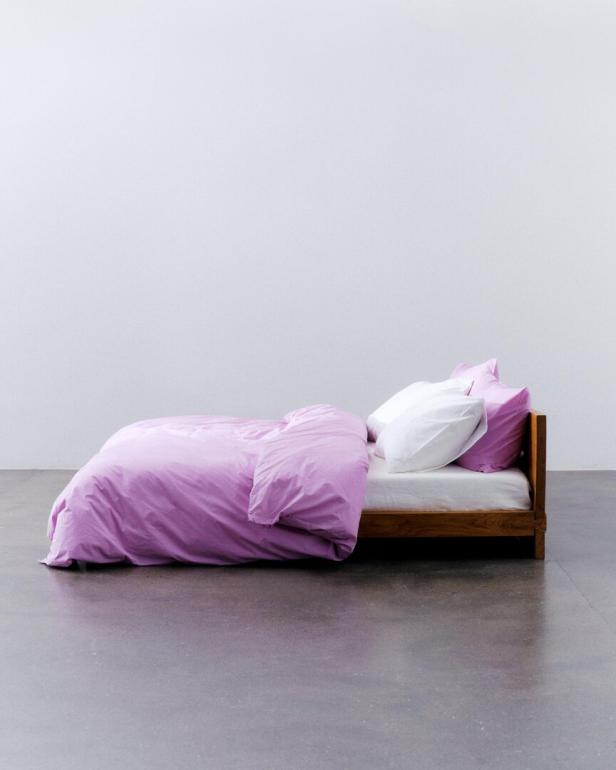 Ein niedriges Bett mit lila Bettwäsche und weißen Kissen steht in einem Raum.