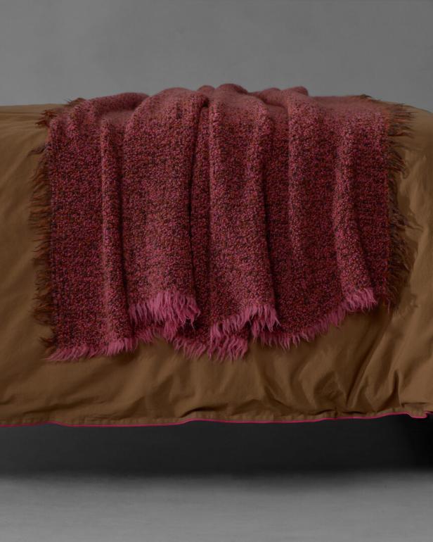 Eine rosa-braune Wolldecke liegt auf einem braunen Bett.