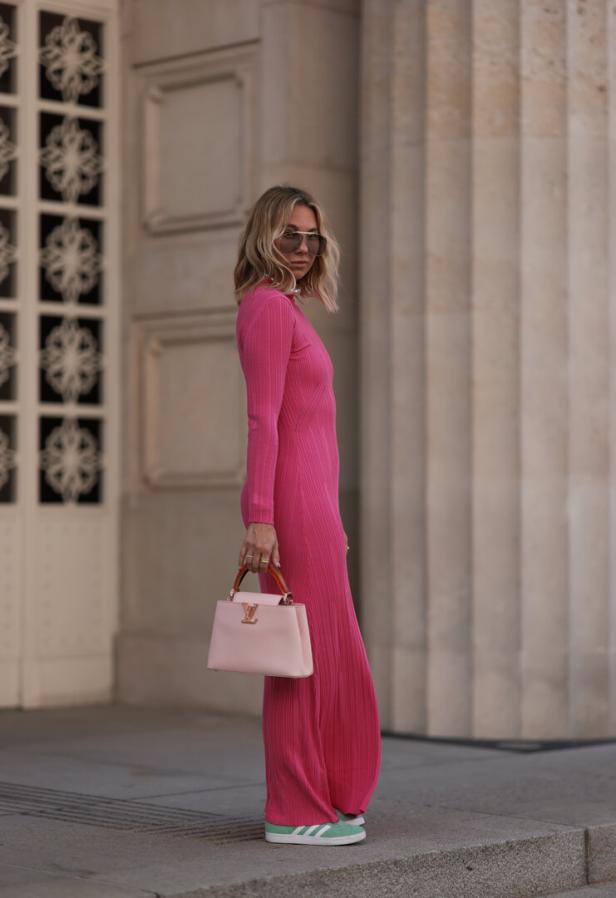 Eine Frau in einem pinkfarbenen Kleid mit einer hellrosa Louis Vuitton Handtasche und grünen Adidas-Sneakers.