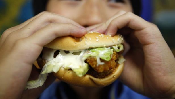 Eine Person hält einen Burger mit Salat und viel Soße in den Händen.