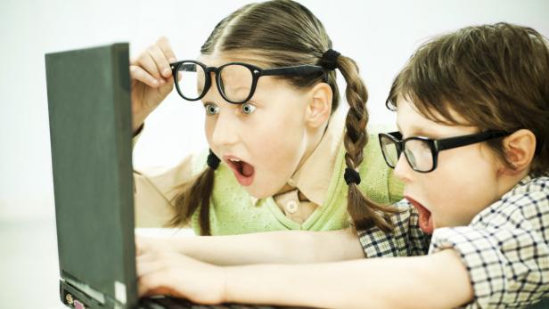 Zwei Kinder mit Brillen schauen überrascht auf einen Laptop.