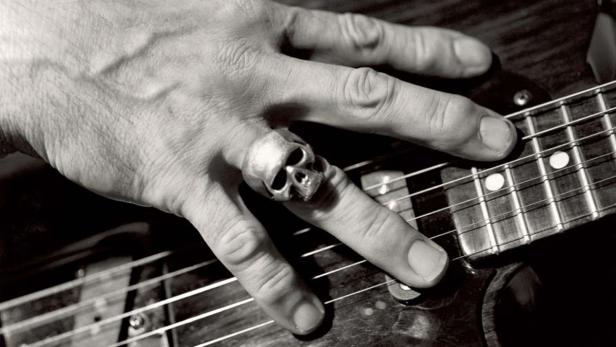 Die Hand eines Gitarristen mit einem Totenkopfring auf einer E-Gitarre.