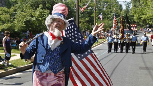 Ein Mann im Uncle-Sam-Kostüm steht mit einer US-Flagge auf einer Parade.