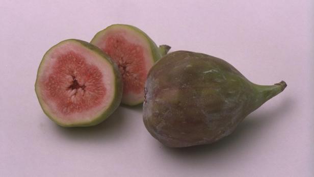 Zwei halbe und eine ganze Feige liegen auf einer hellen Oberfläche.