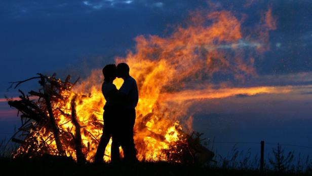 Ein Paar küsst sich vor einem großen Lagerfeuer in der Dämmerung.