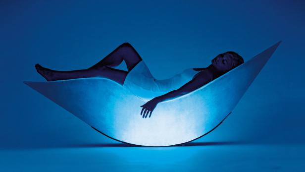 Eine Frau entspannt sich in einem beleuchteten, mondförmigen Sessel.