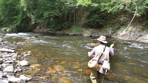 Ein Mann steht in einem Fluss und geht dem Fliegenfischen nach.