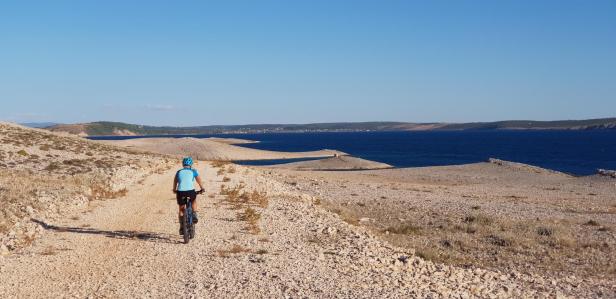 Eine Frau fährt mit dem Mountainbike auf einer Schotterstraße am Meer entlang.