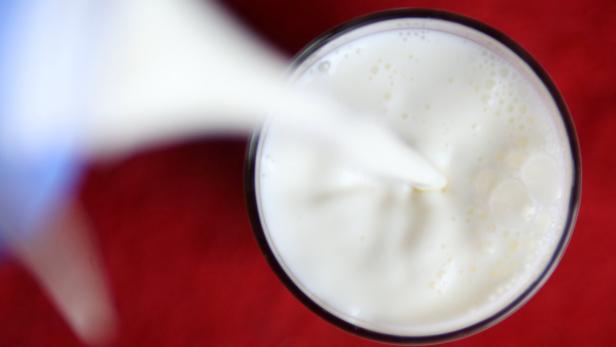 Milch wird in ein Glas auf einem roten Untergrund gegossen.