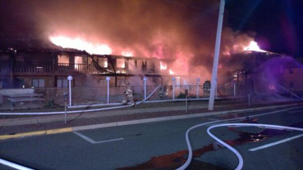 Ein brennendes Gebäude wird von Feuerwehrleuten mit Wasser bespritzt.