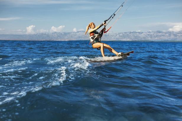 Eine Frau kitesurft auf dem offenen Meer vor einer Bergkulisse.