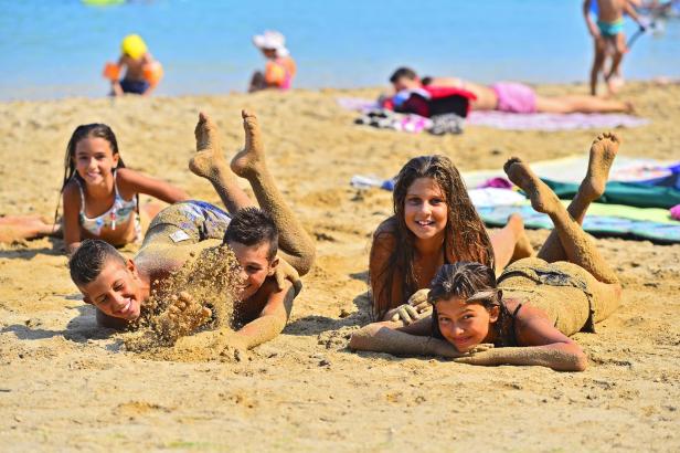 Kinder liegen am Strand und spielen mit Sand.