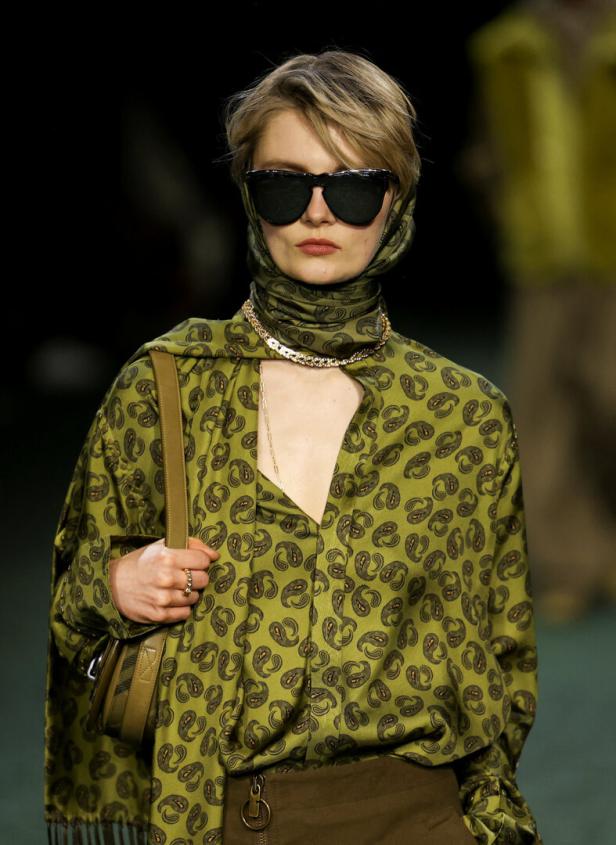 Eine Frau mit Sonnenbrille und einem grün gemusterten Hemd mit passendem Kopftuch.
