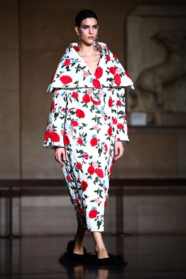 Eine Frau präsentiert ein weißes Kleid mit roten und blauen Blumen auf einem Laufsteg.