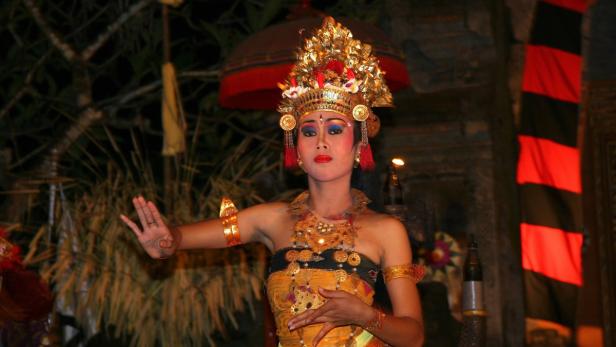 Eine balinesische Tänzerin in traditioneller Kleidung und mit goldenem Kopfschmuck führt einen Tanz auf.