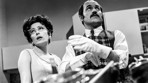 Ein Mann mit Schürze und eine Frau mit Brille schauen nach oben.