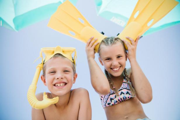 Zwei lachende Kinder posieren mit gelben Schwimmflossen und einer Tauchermaske.