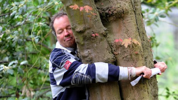 Ein Mann umarmt einen Baum mit geschlossenen Augen.