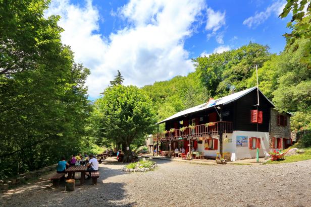 Ein Berghaus mit Gästen im Freien, umgeben von Bäumen.