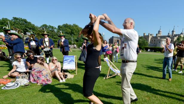 Eine Frau tanzt auf einer Wiese, während eine Blaskapelle spielt und Zuschauer applaudieren.