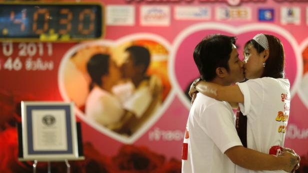 Ein Paar küsst sich vor einem rosafarbenen Hintergrund mit Herzen und einer digitalen Uhr, die 10:30 anzeigt.