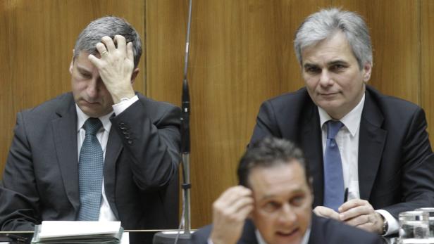 Zwei Männer in Anzügen sitzen an einem Tisch, einer wirkt nachdenklich.