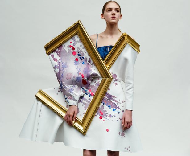Eine Frau trägt ein weißes Kleid, das mit goldenen Rahmen und Farbflecken verziert ist.