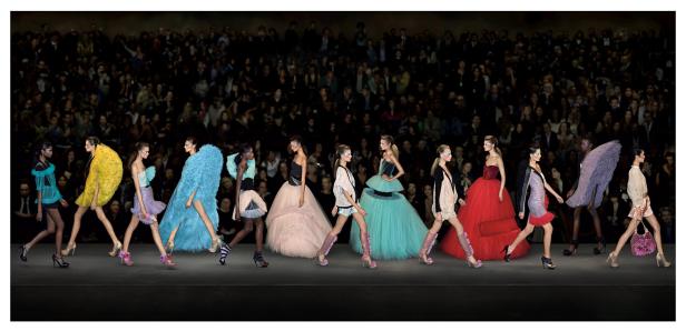 Models präsentieren farbenfrohe Couture-Kreationen auf einem Laufsteg vor einem großen Publikum.