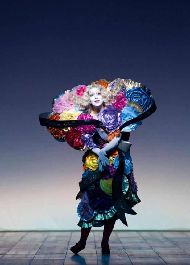 Eine Frau in einem extravaganten, blumenverzierten Kostüm auf einer Bühne.
