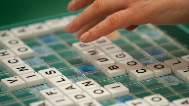 Eine Hand bewegt Spielsteine auf einem Scrabble-Brett.