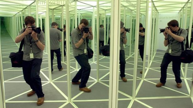 Ein Mann mit einer Kamera steht in einem Spiegelkabinett.