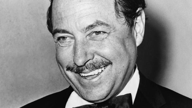 Ein lächelnder Mann mit Schnurrbart und Fliege in Schwarzweiß.