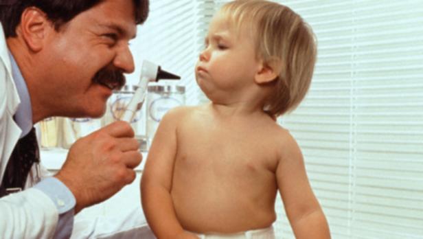 Ein Arzt untersucht ein kleines Kind mit einem Otoskop.