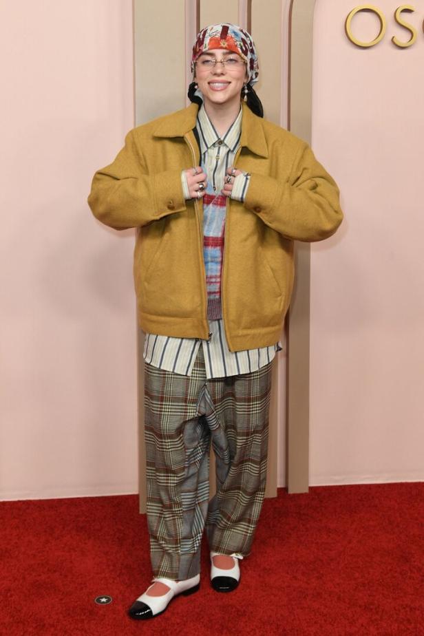 Billie Eilish auf dem roten Teppich in einem übergroßen gelben Jackett, karierter Hose und einem Kopftuch.