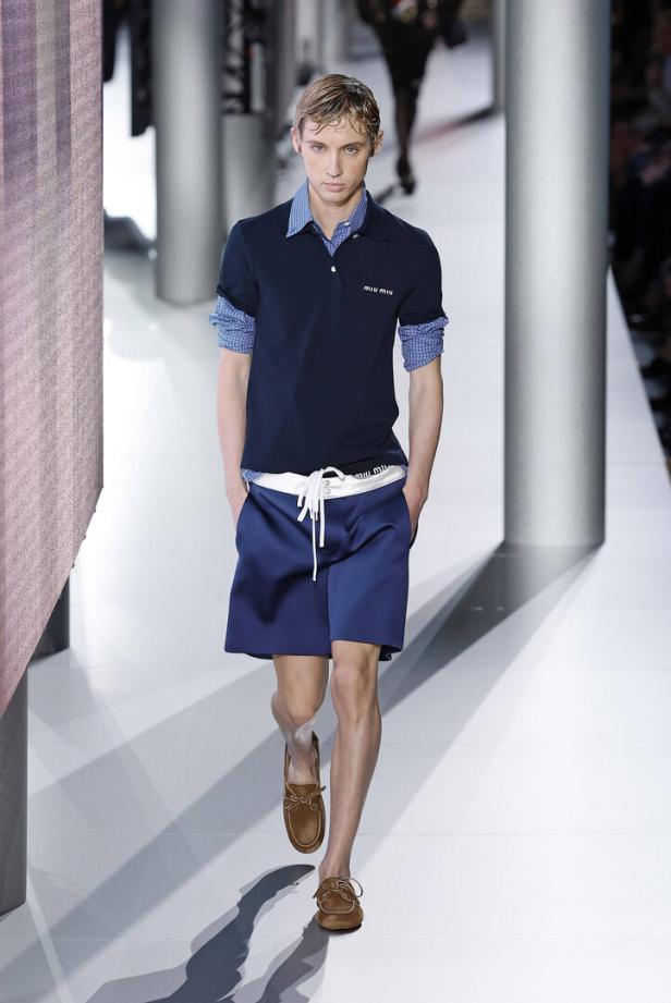 Ein schlanker Mann in einem marineblauen Polohemd und Shorts läuft auf einem Laufsteg.
