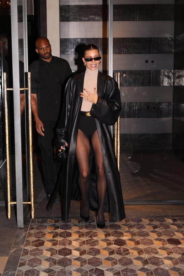 Hailey Bieber verlässt ein Gebäude in einem schwarzen Ledermantel und einer Strumpfhose.