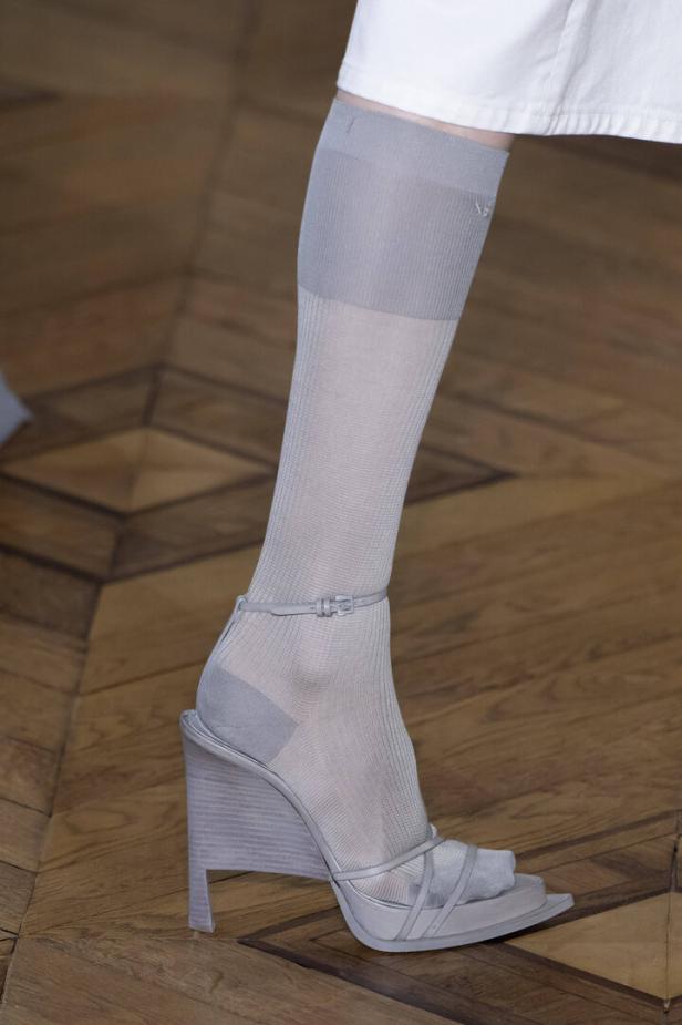 Ein Fuß mit grauen Socken und einem grauen Keilabsatz-Sandalen auf einem Holzboden.