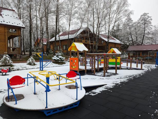 Holzhäuser und ein Kinderspielplatz in einem Wald, alles ist leicht verschneit