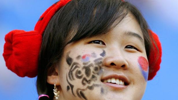 Eine junge Frau mit Gesichtsbemalung und roten Ohrenschützern lächelt.