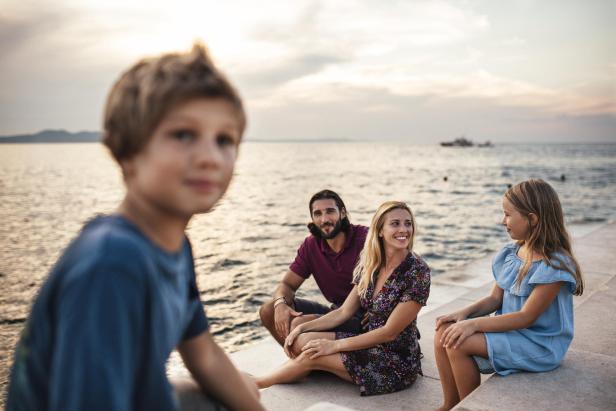 Eine Familie sitzt am Wasser und genießt den Sonnenuntergang.