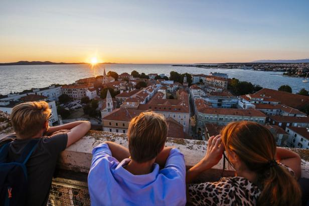 Drei Personen blicken auf die Stadt am Meer bei Sonnenuntergang.