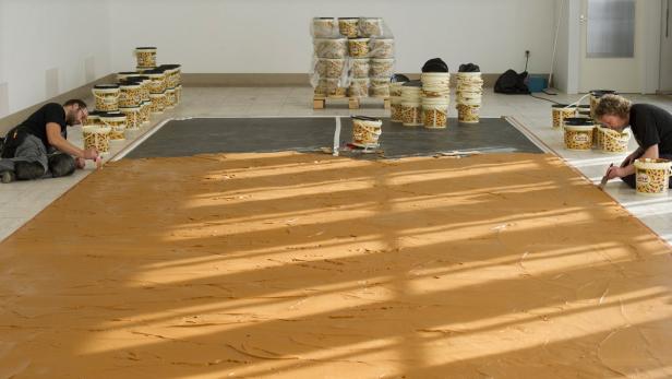 Zwei Personen verteilen Erdnussbutter der Marke Calvé auf dem Boden eines Raumes.