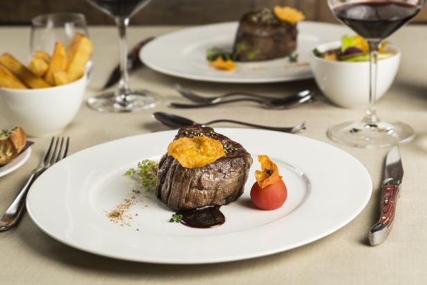 Ein Teller mit einem Filetsteak, garniert mit einer Physalis und einem Chip, auf einem gedeckten Tisch.