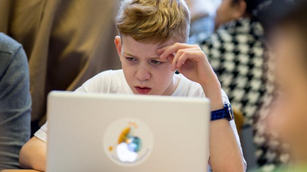 Ein konzentrierter Junge sitzt vor einem Laptop und scheint nachzudenken.