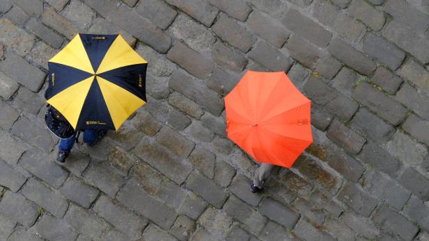 Zwei Personen mit Regenschirmen gehen über einen gepflasterten Weg.