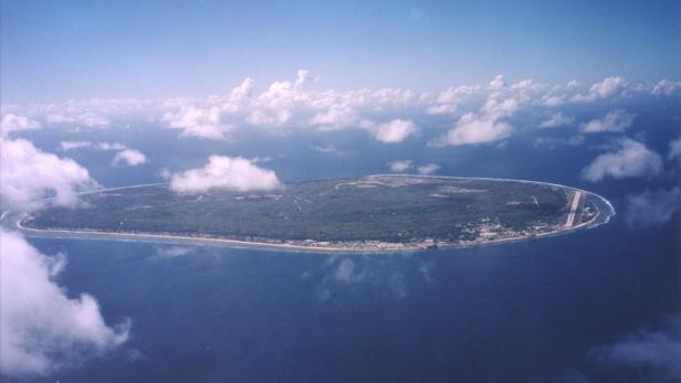 Luftaufnahme einer tropischen Insel mit einem Flugfeld und weißen Wolken am Himmel.