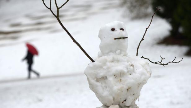 Ein Schneemann mit Ästen als Arme und einer Person mit rotem Regenschirm im Hintergrund.